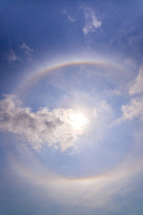 beautiful sun halo with circular rainbow around sun behind blue sky and clouds. fantastic natural phenomenon