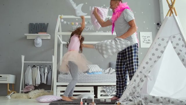 Joyful little girl and her father fighting with pillows