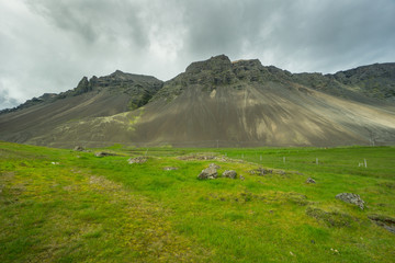 Fototapeta na wymiar Iceland - Moss covered green volcanoe behind meadow with clouds