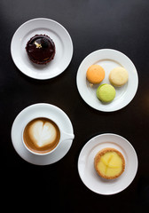 Morning cup of coffee, cake macaron and cake on black background from above. Beautiful breakfast. Flat lay style.

