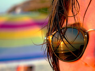 Tramonto riflesso nella lente degli occhiali da sole di una ragazza in spiaggia con ombrellone colorato sullo sfondo