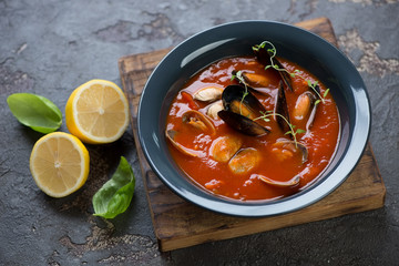 Tomato soup with vongole clams and mussels on a wooden serving board, horizontal shot