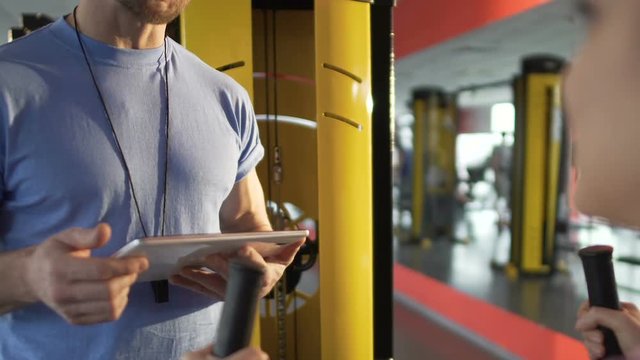 Personal trainer talking to his female trainee, checking information on tablet