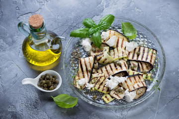 Grilled eggplant and zucchini with olive oil, capers and cheese, gray stone background, studio shot