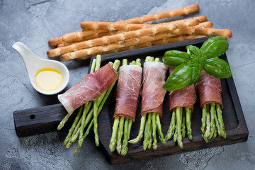 Raw fresh asparagus with prosciutto ham and grissini, gray stone background, studio shot