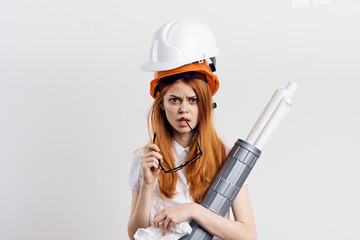Young beautiful woman on a light background holds a paper and drawings, engineer, helmet, construction