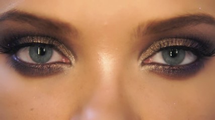 Closeup view of woman's eyes with beautiful golden makeup opening and closing in slowmotion - Powered by Adobe