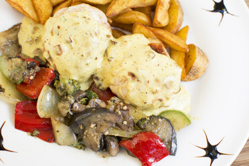 Roasted chicken breast rolls wrapped in bacon slices, served with fried potatoes and cooked vegetables. Topping with the touch of seasoning. Beautifully served plate at the restaurant.