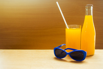 orange juicy drink with blue sunglasses on wood background in summer season concept