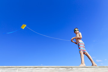 Fototapeta na wymiar Boy with flying kite. boy on the beach playing with a kite on the background of blue sky. Copy space for your text