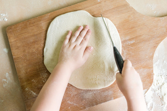children's hands cutting raw rolled dough