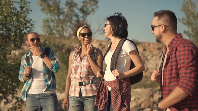 Multiethnic group of people with backpacks talking cheerfully while posing on background of nature.