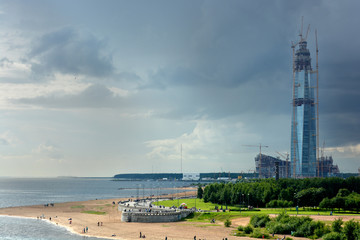 A skyscraper under construction on the seashore under the sky changing from blue to a thunderstorm.