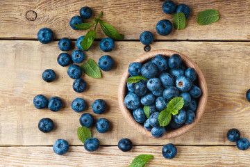 Freshly blueberries green mint leaves in light wooden bowl on rustic table. Bilberry on horizontal planks wooden background. Healthy eating and antioxidant nutrition concept. Top view, copy space.