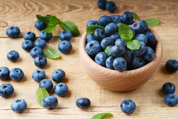 Freshly juicy blueberries with green mint leaves in light wooden bowl on rustic table. Bilberry on horizontal wooden background. Healthy eating and antioxidant nutrition concept. Top view.
