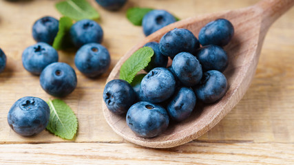 Freshly picked juicy blueberries, green mint leaves wooden spoon rustic table. Bilberry on horizontal wooden background. Healthy eating antioxidant nutrition concept. Close up, selective focus.