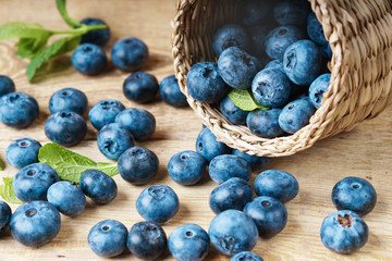 Freshly picked juicy blueberries green mint leaves light wooden bowl rustic table. Bilberry wooden background. Healthy eating and antioxidant nutrition concept. Selective focus, close up.