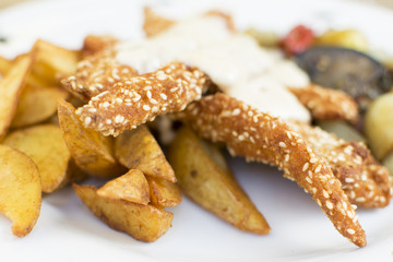 Delicious sesame chicken sticks with potatoes and vegetables. Delicious buttery topping. Beautifully served plate at the restaurant.