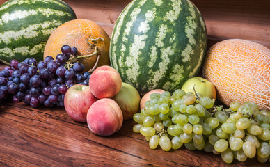 Watermelons, melons, grapes, apples and peaches on the background of wood texture. Still life with...