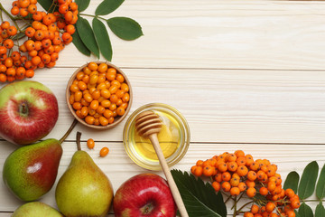 Sea buckthorn in wooden bowl, honey, rowan, apple, pear on wooden table. top view with copy space
