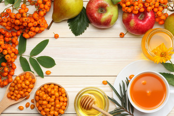 Sea buckthorn in wooden bowl, honey, rowan, apple, pear on wooden table. top view with copy space