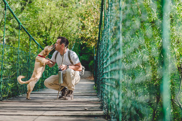 Hiker with dog resting on wooden suspension bridge