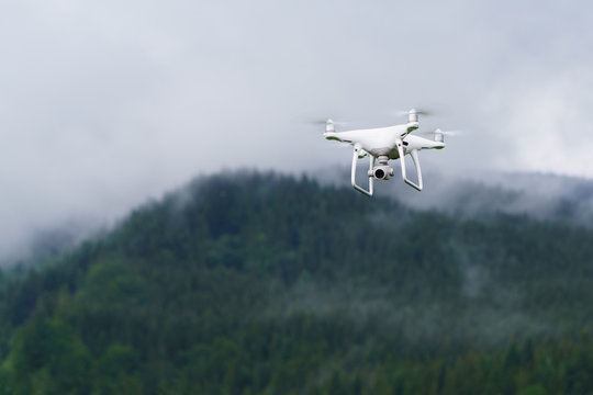 White professional camera drone takes pictures.  Professional copter. Horizontal mountains landscape quadcopter background, copy space, selective focus.