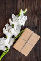 To wrap a gift. Box in kraft paper near flower gladiolus on dark wooden table top view