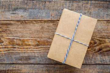 Fototapeta premium To wrap a gift. Box in kraft paper on rustic wooden background top view copyspace