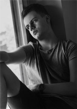 distressed teenager boy sitting on window