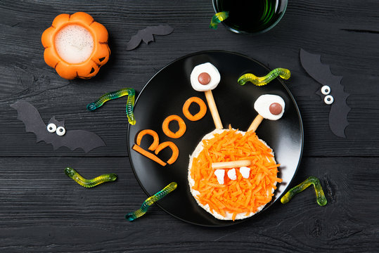 Funny toast with carrots in a shape of monster and gummy candies worms, sandwich for kids Halloween idea, top view on wooden background
