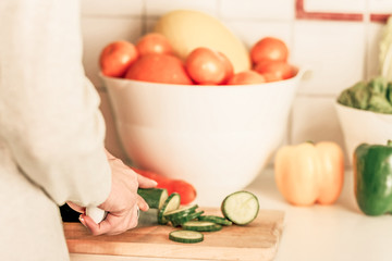 Young caucasian woman is cutting cucumber.