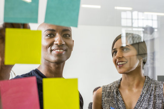 Woman and man reading adhesive notes in office - Powered by Adobe