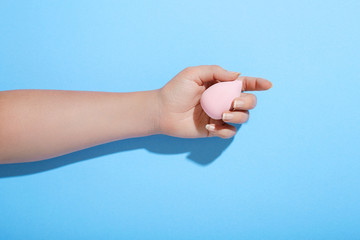 Woman's hand holding makeup sponge on blue background