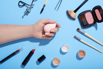 Makeup and female hand holding makeup sponge on blue background