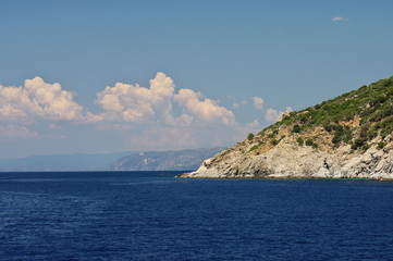 Fototapeta na wymiar Athos peninsula, Greece. Steep edges of Athos peninsula. Blue sky with white clouds over the azure sea.