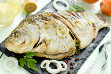 Fried fish with onion and herbs on black stone plate