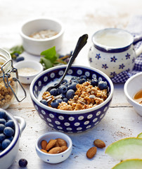 Granola with natural yogurt, fresh blueberries, nuts and honey in a ceramic bowl on a white wooden table. Delicious breakfast or dessert.  Healthy eating concept.