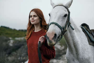 Fototapeta premium Young beautiful woman in the mountains with a white horse