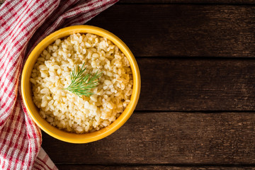 Bulgur with dill in yellow ceramic bowl on dark wooden background
