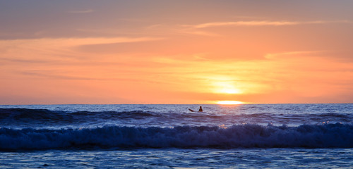 Surfer waiting for the next wave at sunset