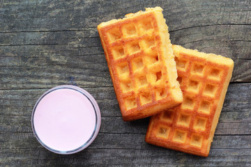 Glass of raspberry yogurt and two freshly baked wafers waffles on old grey wooden table, top view