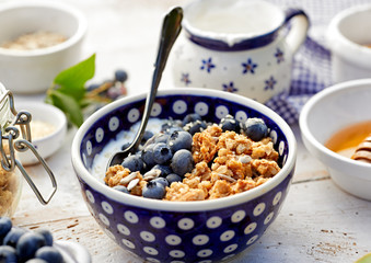 Granola with natural yogurt, fresh blueberries, nuts and honey in a ceramic bowl on a white wooden table, close up. Delicious breakfast or dessert.  Healthy eating concept.