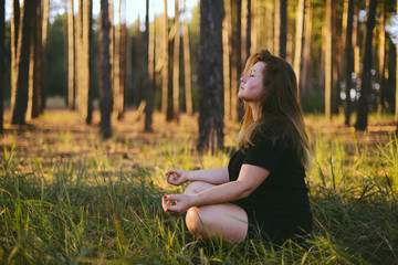 Middle aged woman sitting in lotus position in forest. her eyes are closed. Middle-aged woman in her 40s meditating for exercise outdoors