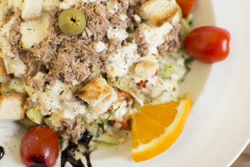 Tuna salad with lettuce, olives, and tomatoes. Orange decoration on a white plate.