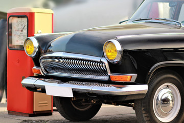 Frontal part of an old vintage black car with blurred background near retro red gas station