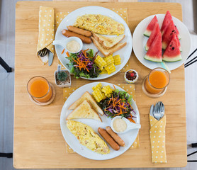 Top view of omelet with orange juice, watermelon, croissants, cereals and fruits on wooden table. Balanced diet.