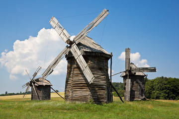 Fototapeta na wymiar Three wooden log windmills in the field at sunny day