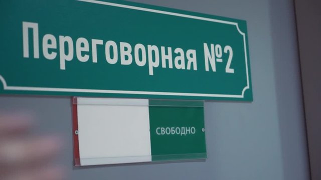 Unrecognisable female hand moves plate from free to occupied on door with green plastic sign russian text meeting room