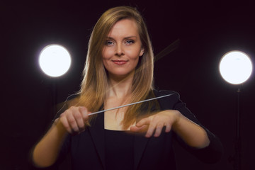 Young caucasian woman conductor poses with baton in a dark space with stage lights